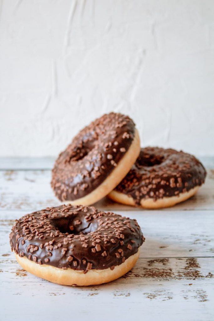 Close-up of chocolate glazed donuts with sprinkles on a rustic wooden table.