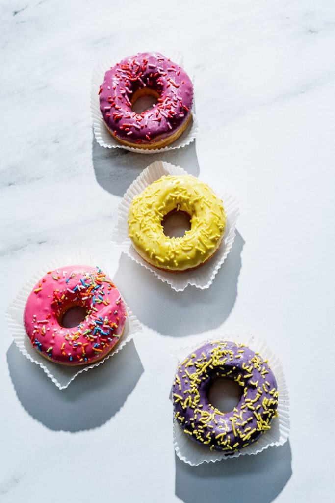 A vibrant array of glazed donuts with sprinkles on a marble surface, shot in a flat lay style.
