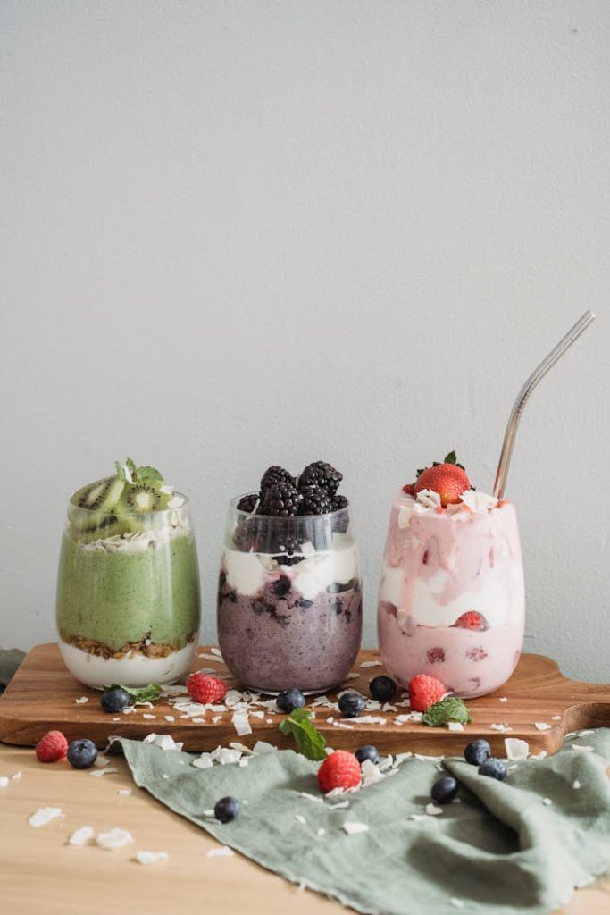 Accueil Three colorful fruit smoothies with yogurt and berries on a wooden board, perfect for a healthy snack.